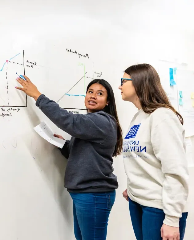 A student explains a drawing of a graph on a whiteboard to another student